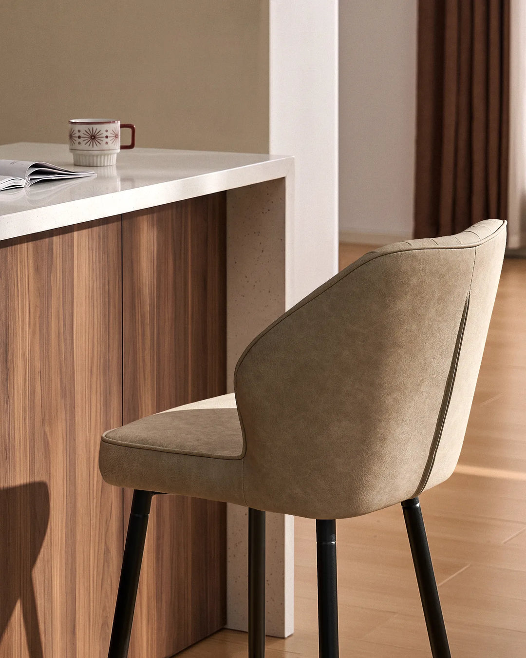 Close-up of a Danforth beige bar stool showing its softly curved backrest, padded seat, vertical channel stitching and black metal legs