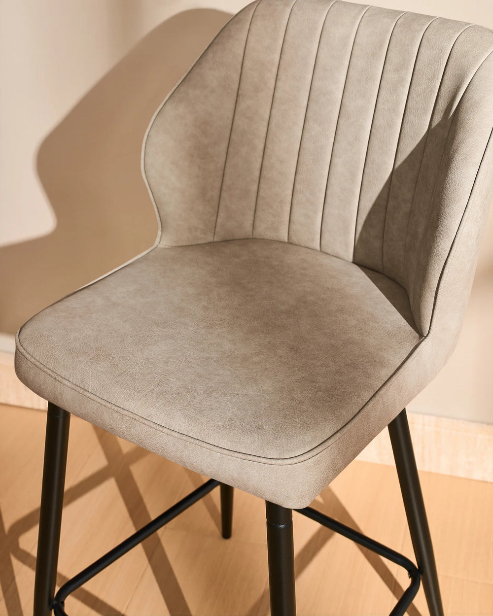 Front view close-up of a Danforth beige bar stool highlighting the curved upholstered backrest, vertical stitched detailing and cushioned seat