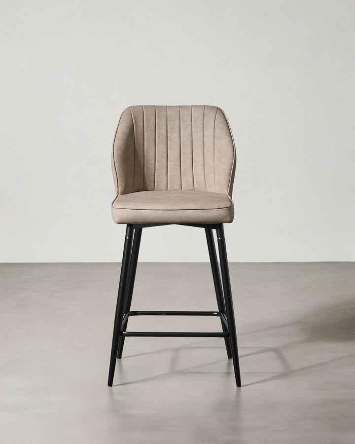 Front view of a Danforth beige bar stool with a curved padded backrest, upholstered seat and slim black metal legs