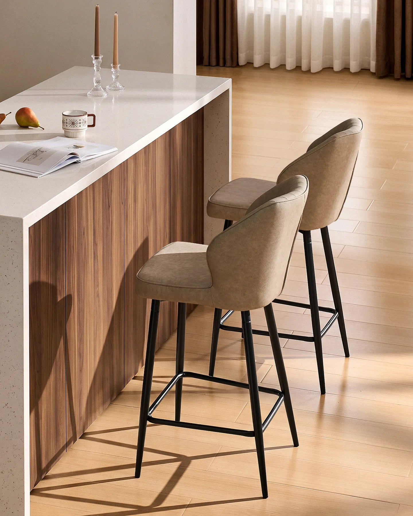 Side view of two Danforth beige bar stools showing the curved upholstered backrests, slim black metal legs and footrests at a kitchen island