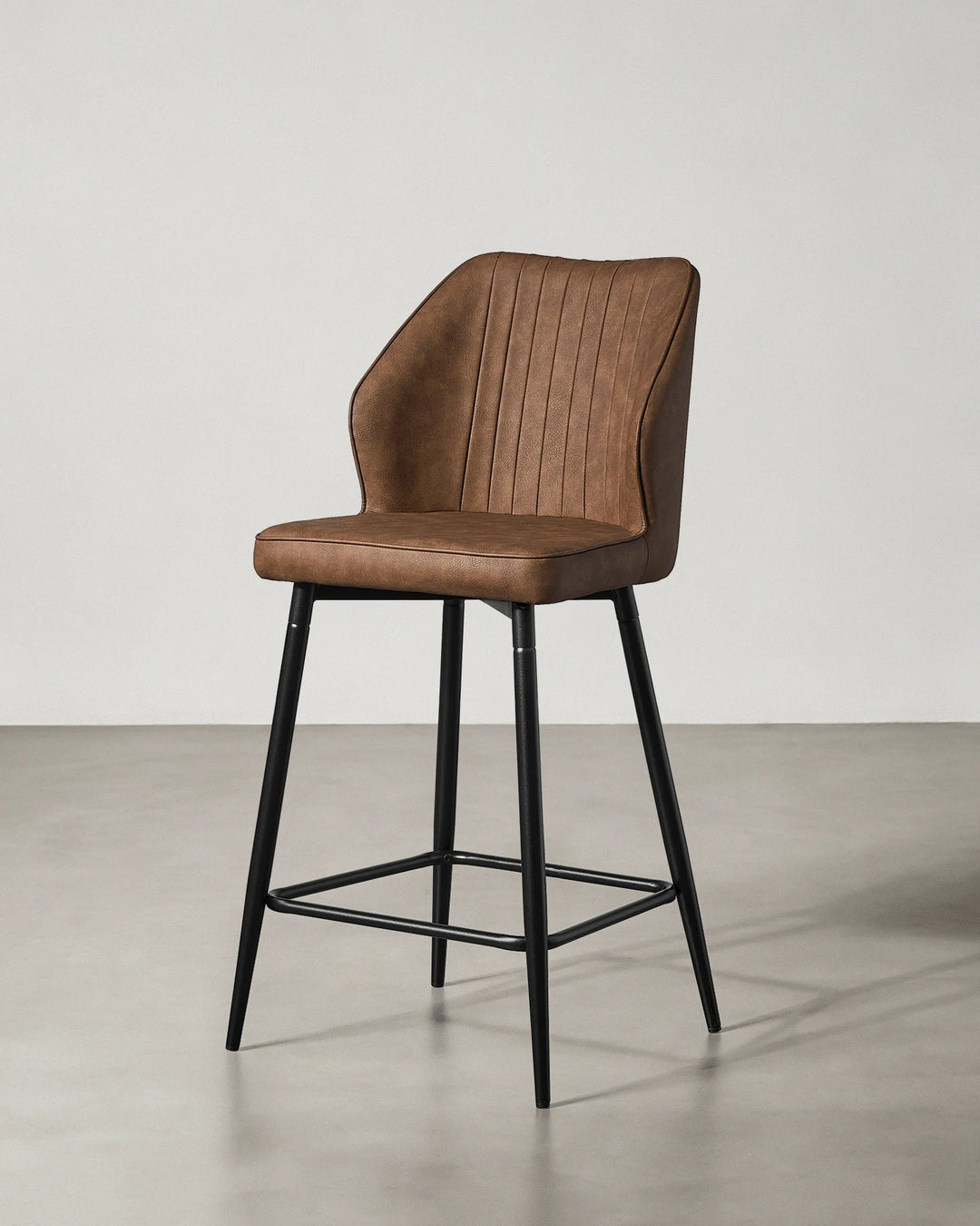 Three-quarter view of a Danforth Brown bar stool showing the upholstered seat and backrest with vertical channel stitching and black metal frame