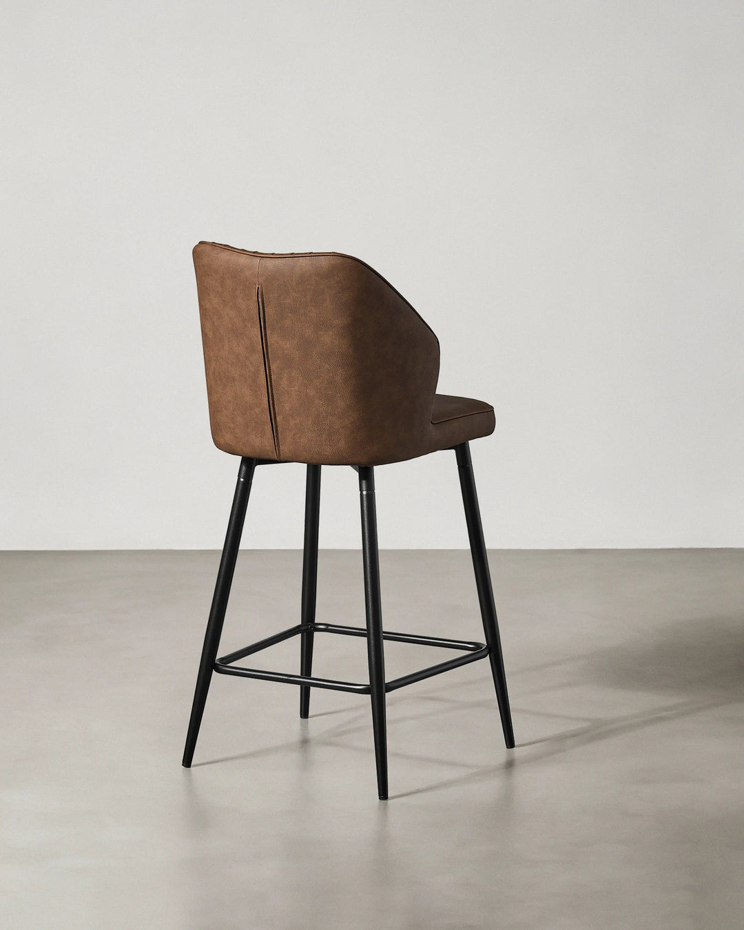 Rear view of a Danforth Brown bar stool showing the upholstered backrest, curved silhouette and black metal frame