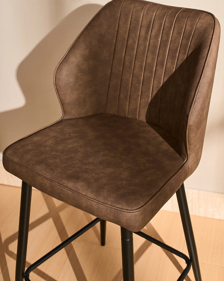 Side view close-up of a Danforth Brown bar stool highlighting the curved upholstered backrest, vertical stitched detailing and cushioned seat