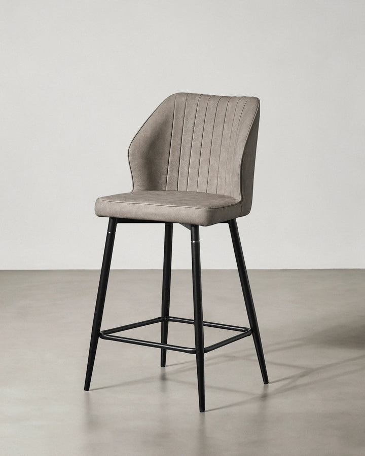 Three-quarter view of a Danforth Light Grey bar stool showing the upholstered seat and backrest with vertical channel stitching and black metal frame
