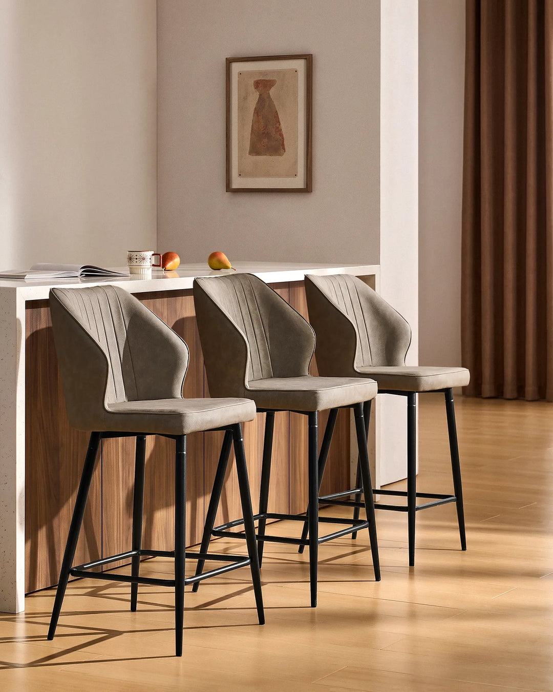 Three Danforth Light Grey bar stools arranged along a contemporary kitchen island, featuring upholstered seats, vertical stitching and black metal frames