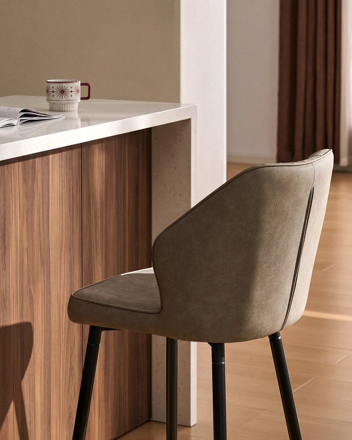 Close-up of a Danforth Light Grey bar stool showing its softly curved backrest, padded seat, vertical channel stitching and black metal legs