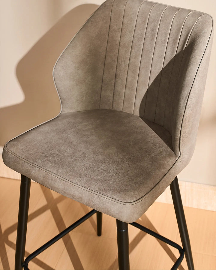 Side view close-up of a Danforth Light Grey bar stool highlighting the curved upholstered backrest, vertical stitched detailing and cushioned seat