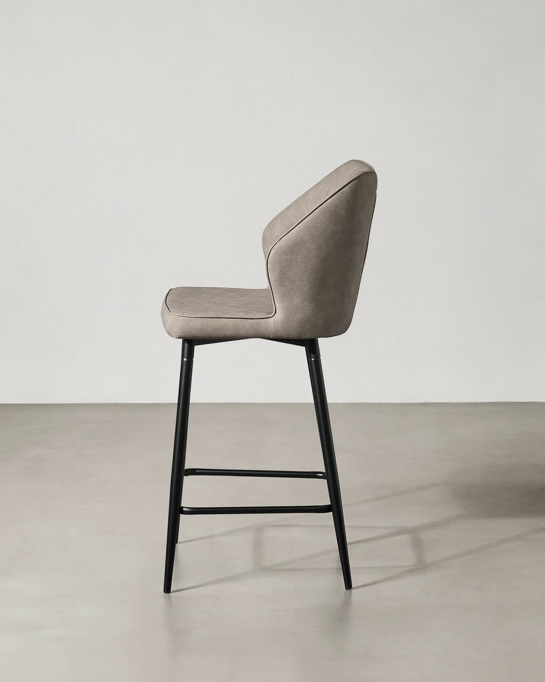 Side profile of a Danforth Light Grey bar stool showing the gently curved upholstered back, cushioned seat and slim black metal legs
