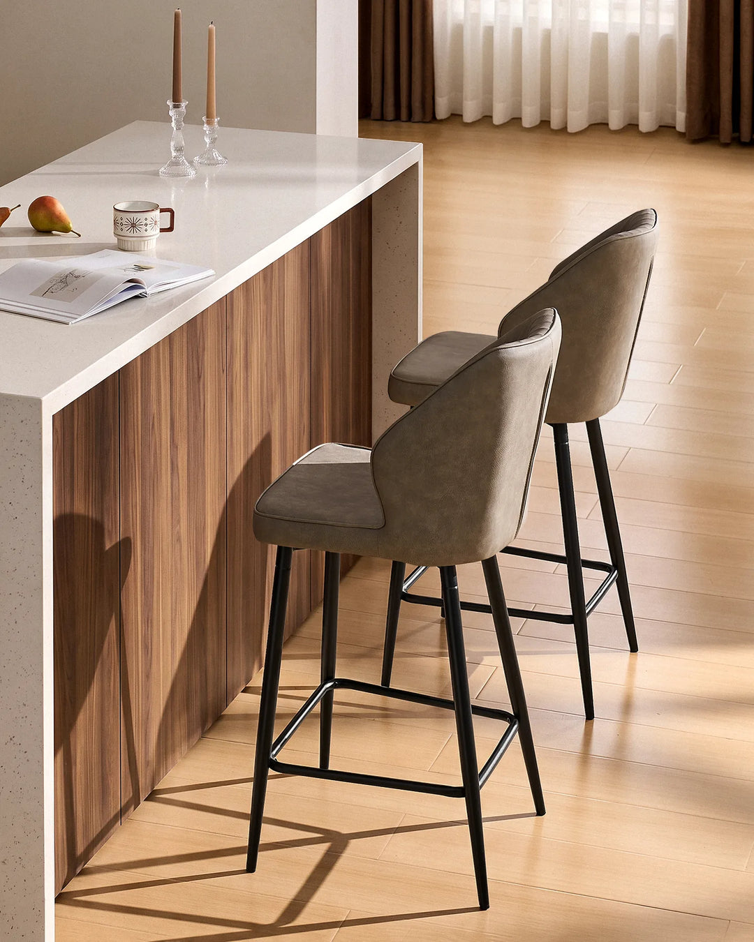 Side view of two Danforth Light Grey bar stools showing the curved upholstered backrests, slim black metal legs and footrests at a kitchen island