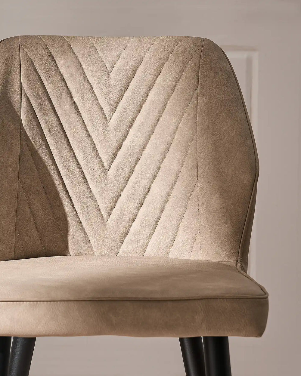 Detailed view of the beige dining chair backrest, showcasing the distinctive V-shaped stitched pattern and upholstered finish.