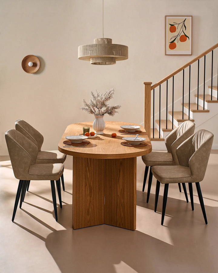 Beige dining chairs arranged around a round wooden dining table, complemented by warm lighting, framed artwork and a staircase.