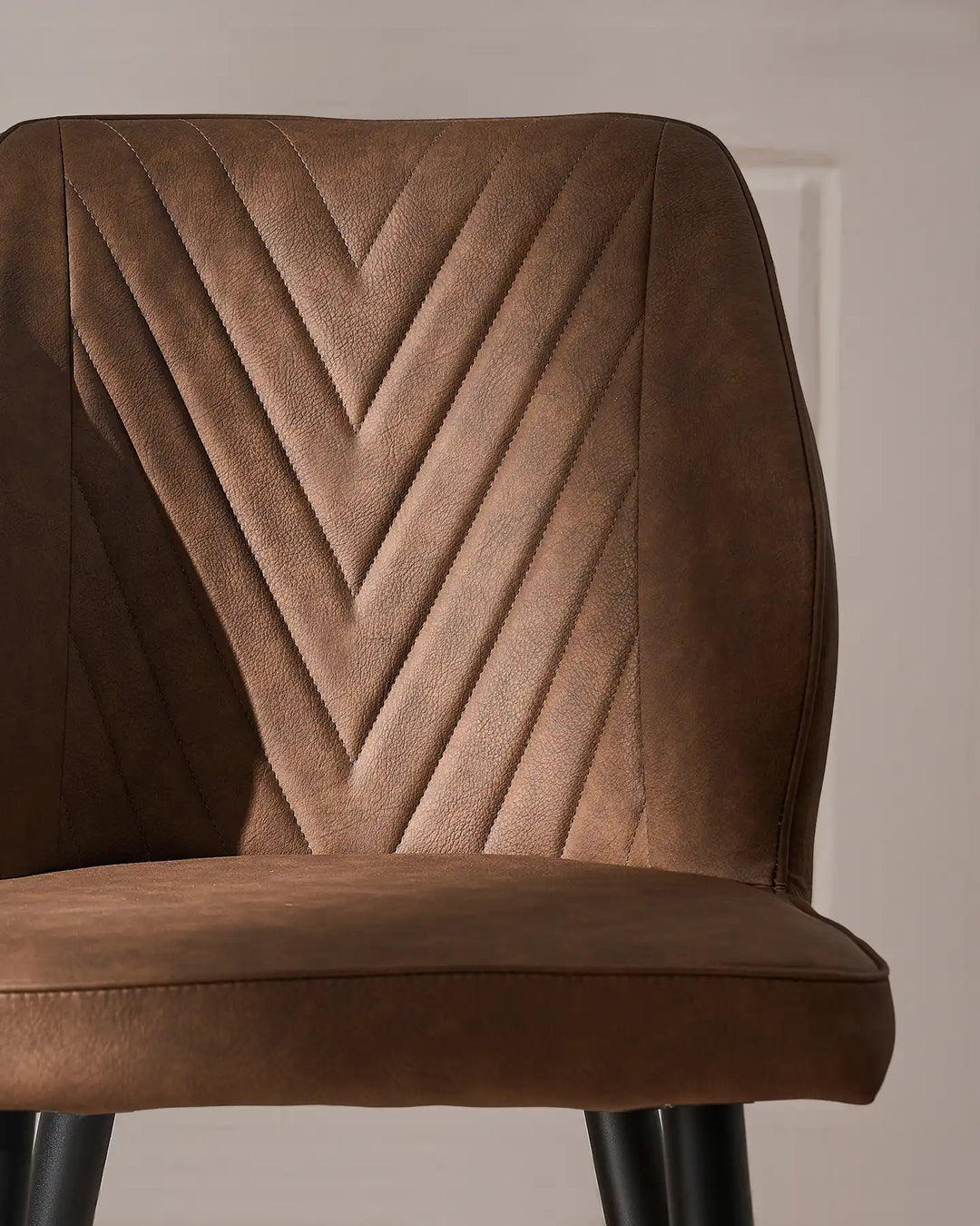 Detailed view of the brown dining chair backrest, showcasing the distinctive V-shaped stitched pattern and upholstered finish.