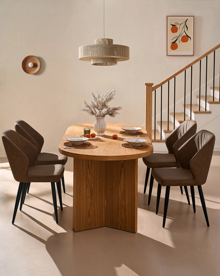 Brown dining chairs arranged around a round wooden dining table, complemented by warm lighting, framed artwork and a staircase.