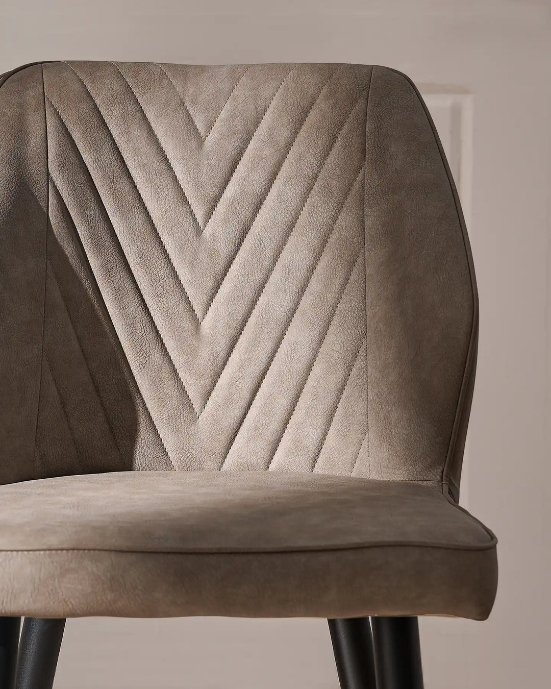 Detailed view of the grey dining chair backrest, showcasing the distinctive V-shaped stitched pattern and upholstered finish.
