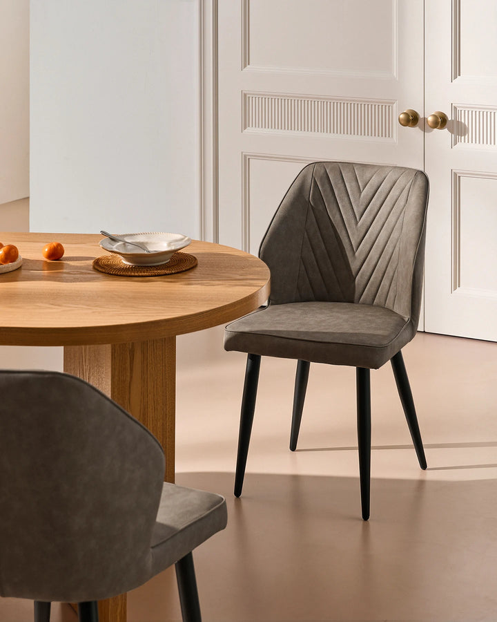 Grey faux leather dining chair beside a wooden dining table, styled with neutral interiors and classic wall panelling.