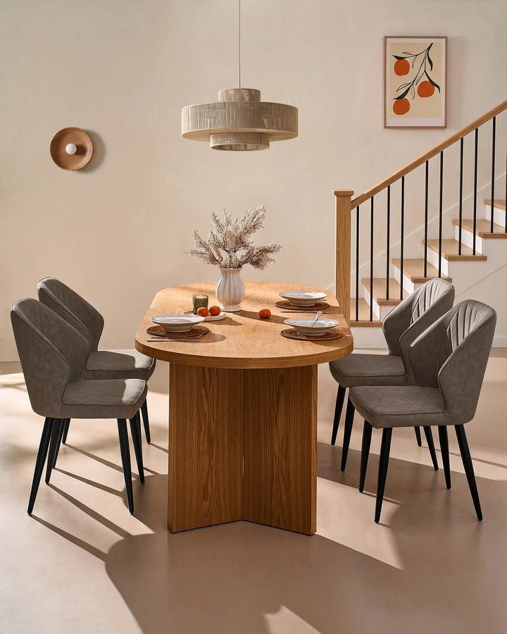 Grey dining chairs arranged around a round wooden dining table, complemented by warm lighting, framed artwork and a staircase.