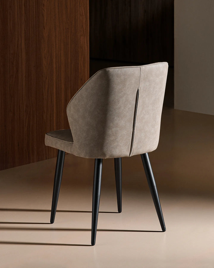 Rear view of the Daviyon grey dining chair, showing its curved upholstered back and slim black metal legs against a warm wood-effect backdrop.