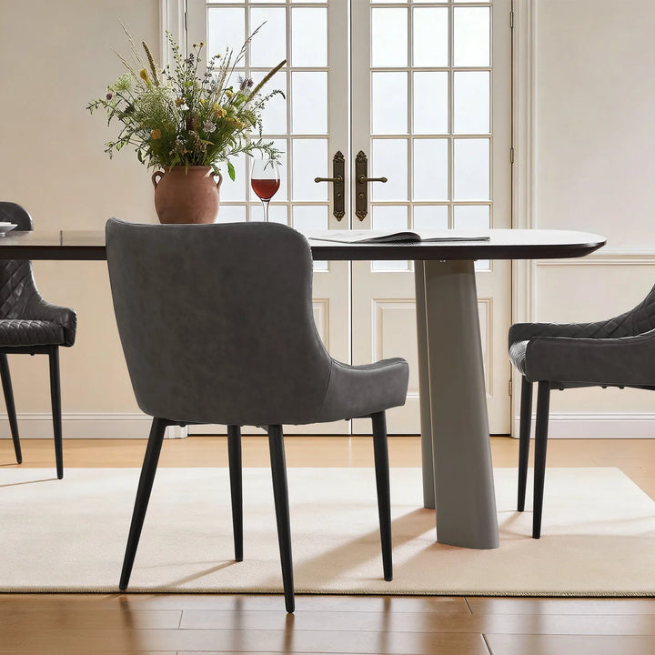 Three grey faux leather dining chairs surrounding a dining table, highlighting the smooth curved back design
