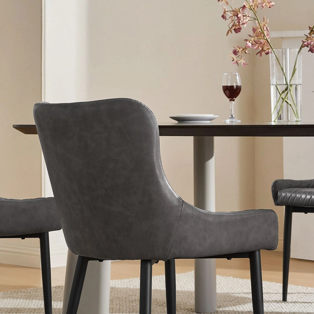 Three grey faux leather dining chairs surrounding a dining table, highlighting the smooth curved back design
