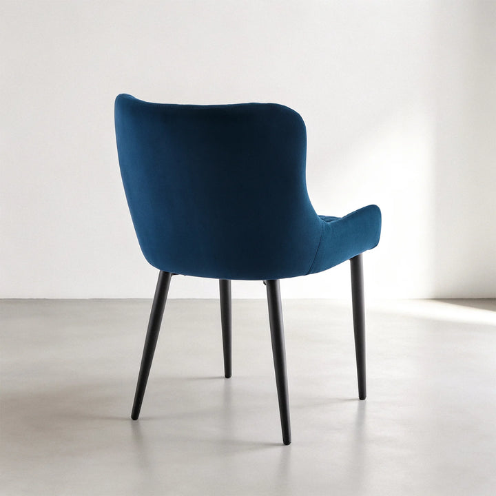 Back view of a Dundas blue velvet dining chair showing the curved upholstered backrest and four slim black metal legs