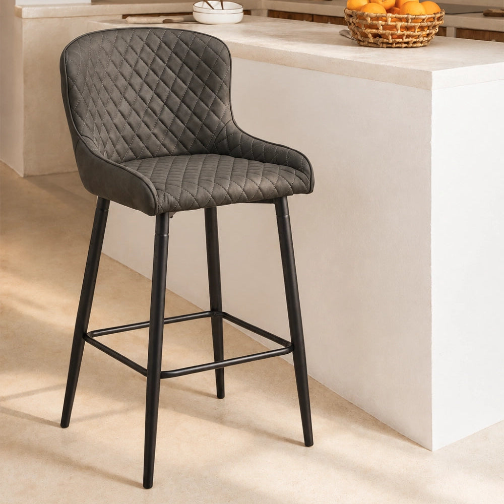 Dundas Faux Leather Bar Stools beside a kitchen island, featuring diamond stitches, a curved back and black metal legs