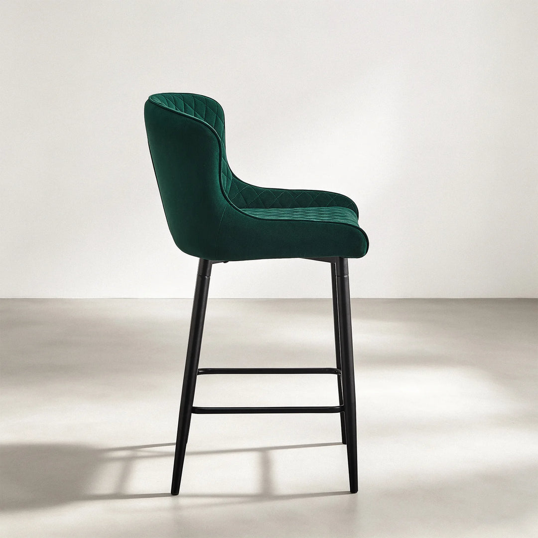 Side profile of Dundas green velvet bar stool showing the curved seat, high backrest and black metal legs