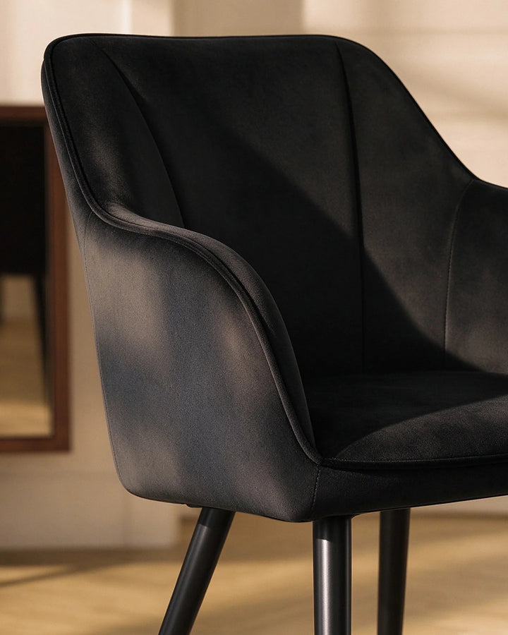 Close-up of the Earven black velvet dining chair highlighting its sculpted curved backrest, padded armrest and soft upholstered finish