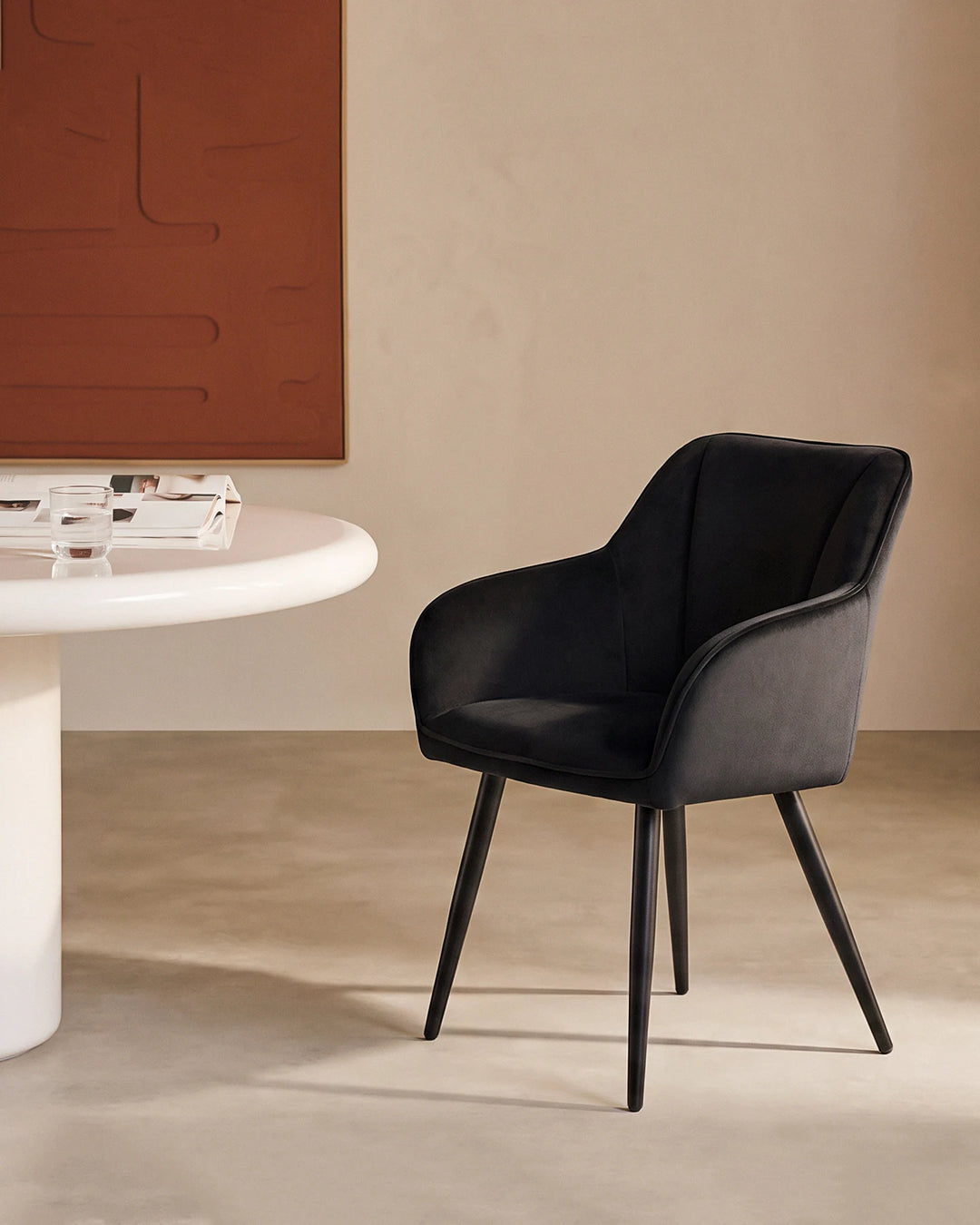 Earven black velvet dining chair styled beside a white dining table in a warm neutral dining space