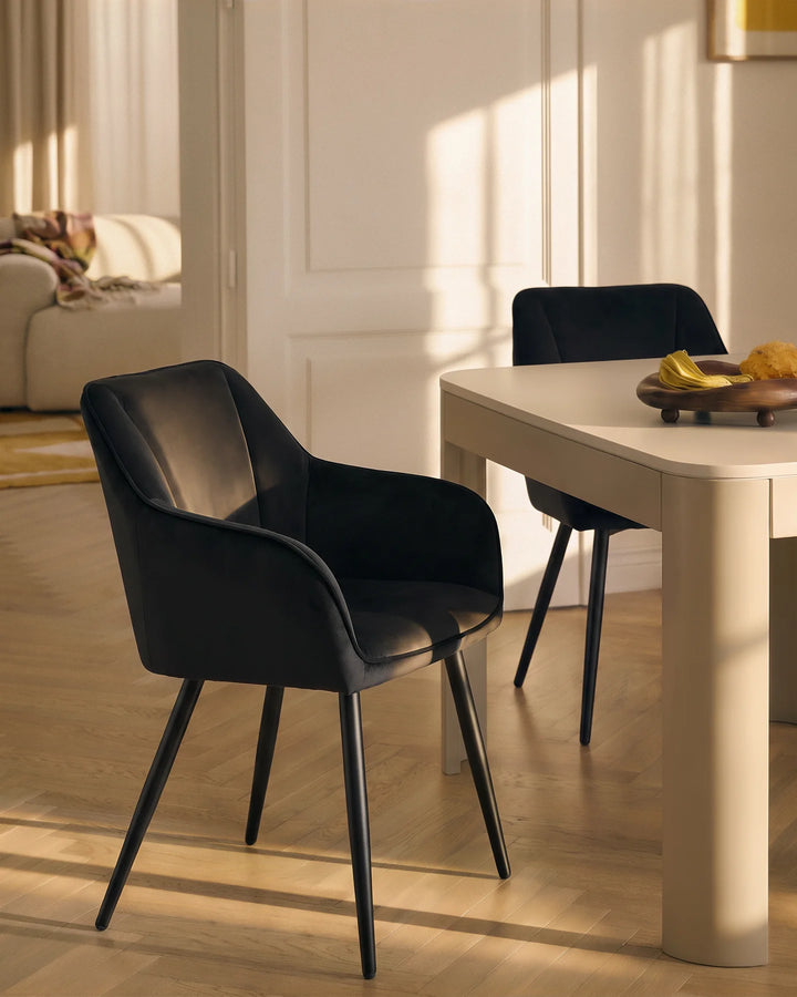 Black velvet dining chairs arranged around a round dining table in a contemporary neutral dining room with wooden flooring and a display cabinet