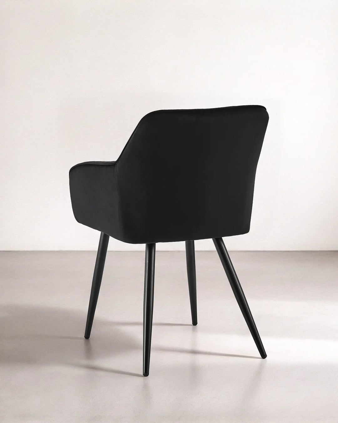 Rear view of the Earven black velvet dining chair showing its smooth upholstered back, curved silhouette and tapered black metal legs