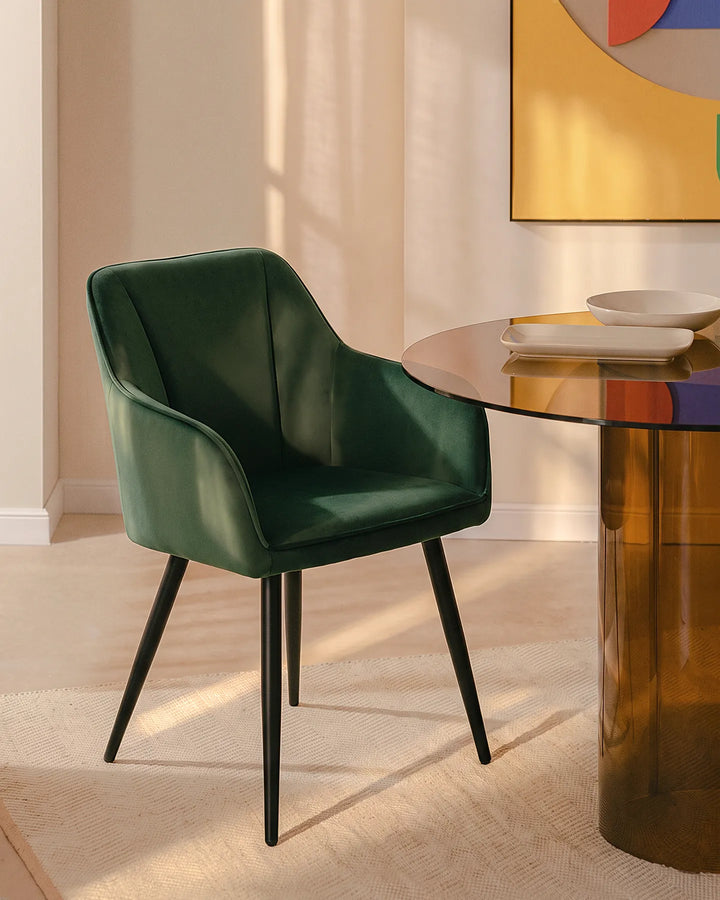 Earven green velvet dining chair styled beside a wooden dining table in a warm neutral dining space with framed wall art and full-length curtains
