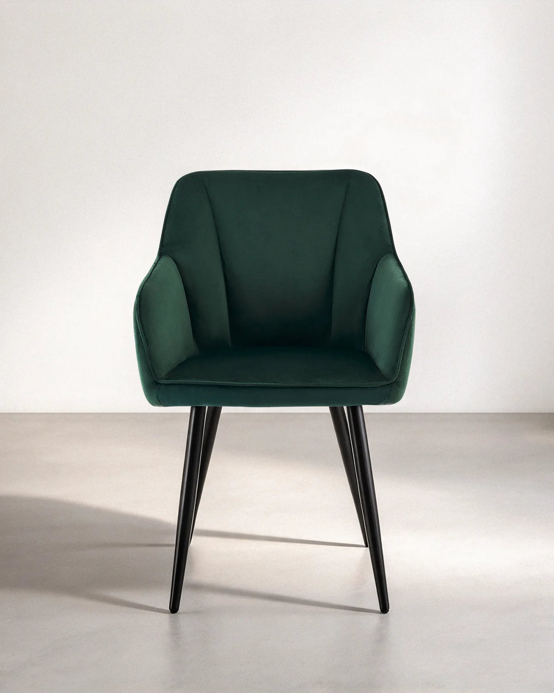 Front view of the Earven green velvet dining chair featuring a softly curved backrest, integrated armrests, plush seat cushion and black metal legs