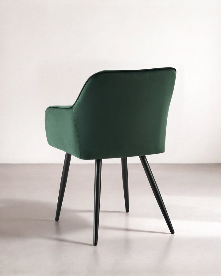 Rear view of the Earven green velvet dining chair showing its smooth upholstered back, curved silhouette and tapered black metal legs