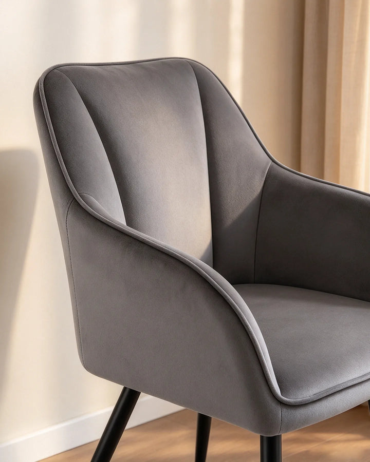 Close-up of the Earven grey velvet dining chair highlighting its sculpted curved backrest, padded armrest and soft upholstered finish
