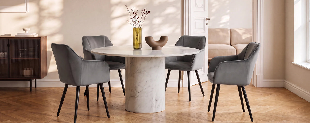 Earven grey velvet dining chairs arranged around a round dining table in a warm contemporary dining room with a neutral sofa, wooden flooring and natural decorative accents