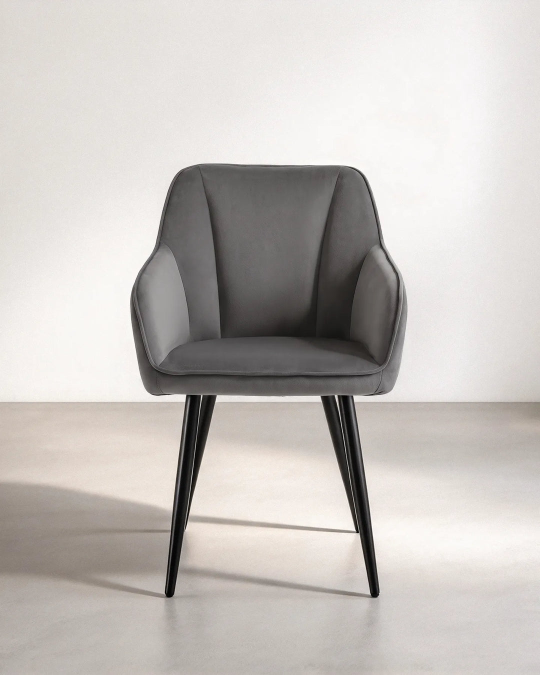 Front view of the Earven grey velvet dining chair featuring a softly curved backrest, integrated armrests, plush seat cushion and black metal legs