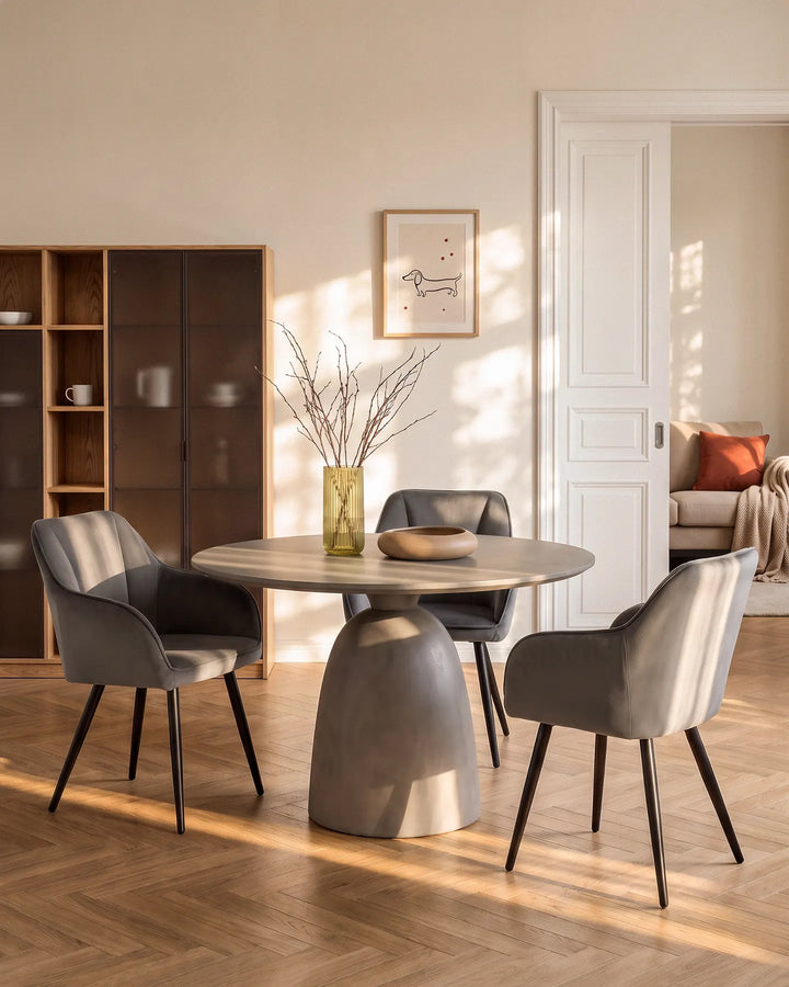 Grey velvet dining chairs arranged around a round dining table in a contemporary neutral dining room with wooden flooring and a display cabinet