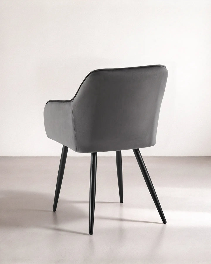 Rear view of the Earven grey velvet dining chair showing its smooth upholstered back, curved silhouette and tapered black metal legs
