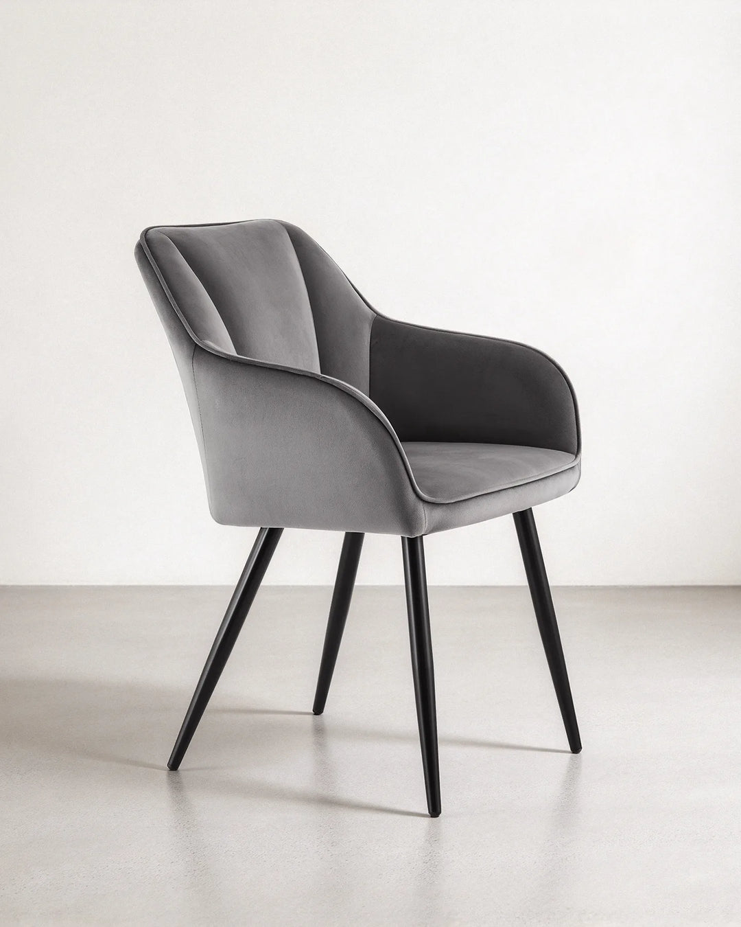 Side profile of the Earven grey velvet dining chair highlighting its wraparound backrest, supportive armrests, cushioned seat and slim black legs
