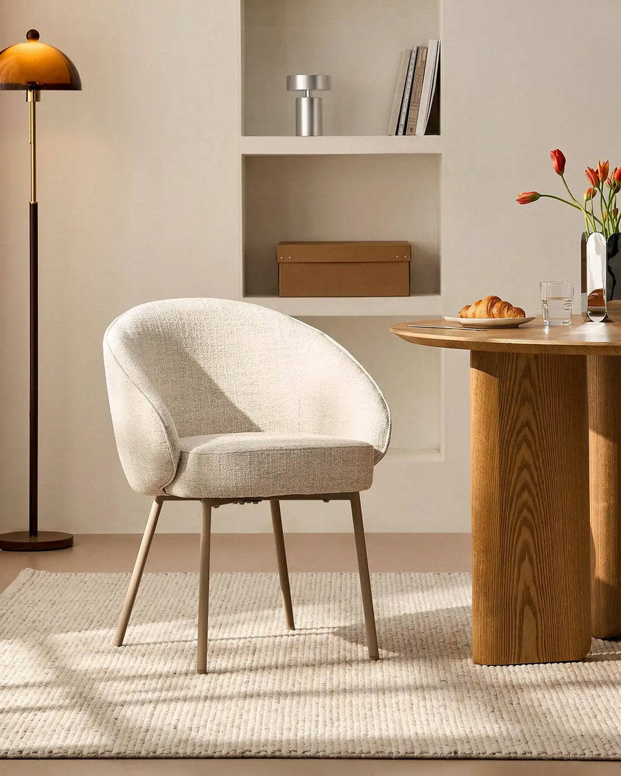 Front view of the Elowen beige linen dining chair beside a dining table with thick padded comfort and elegant curved backrest