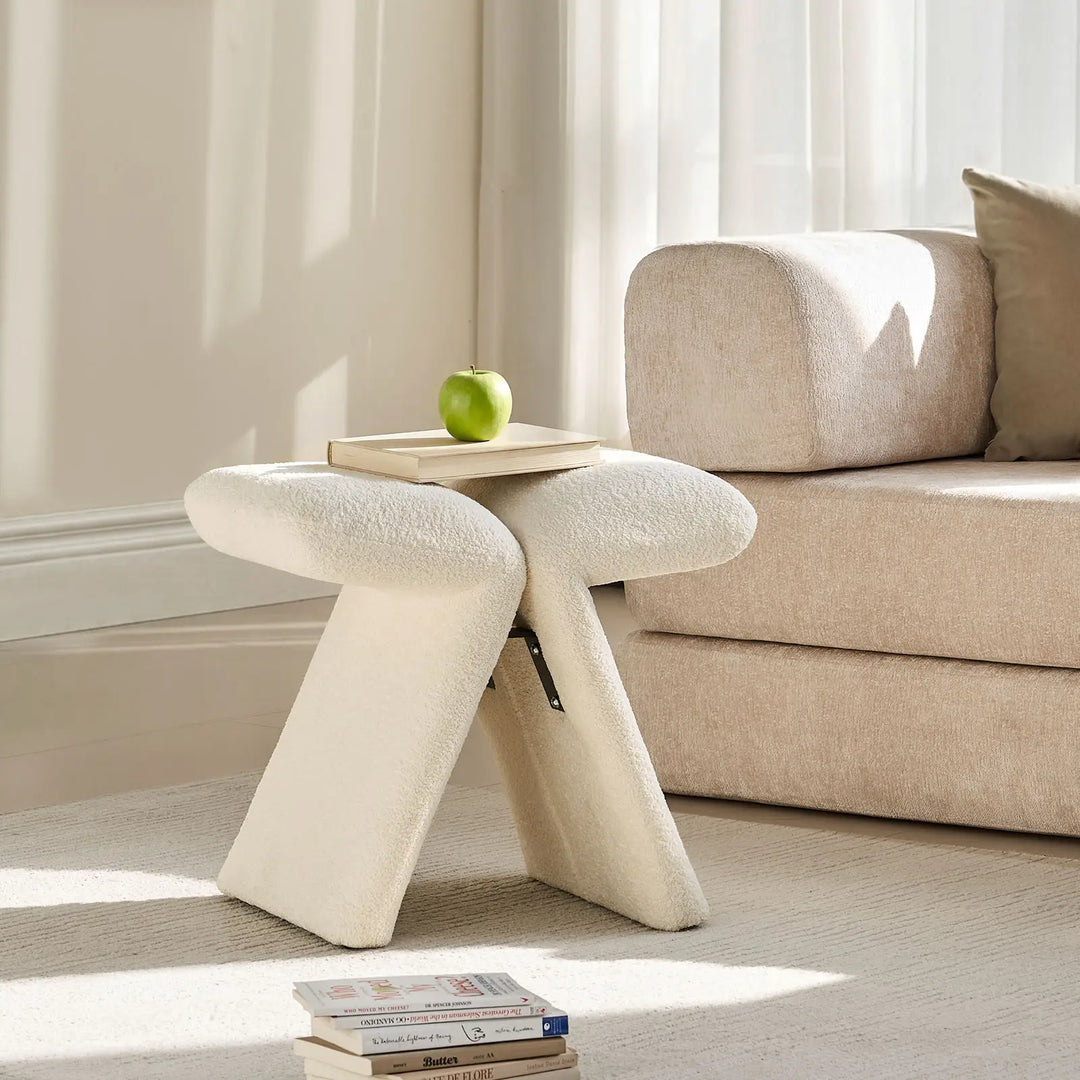 Faye warm white Accent Stool styled beside a sofa in a modern living room, used as a side stool with books.