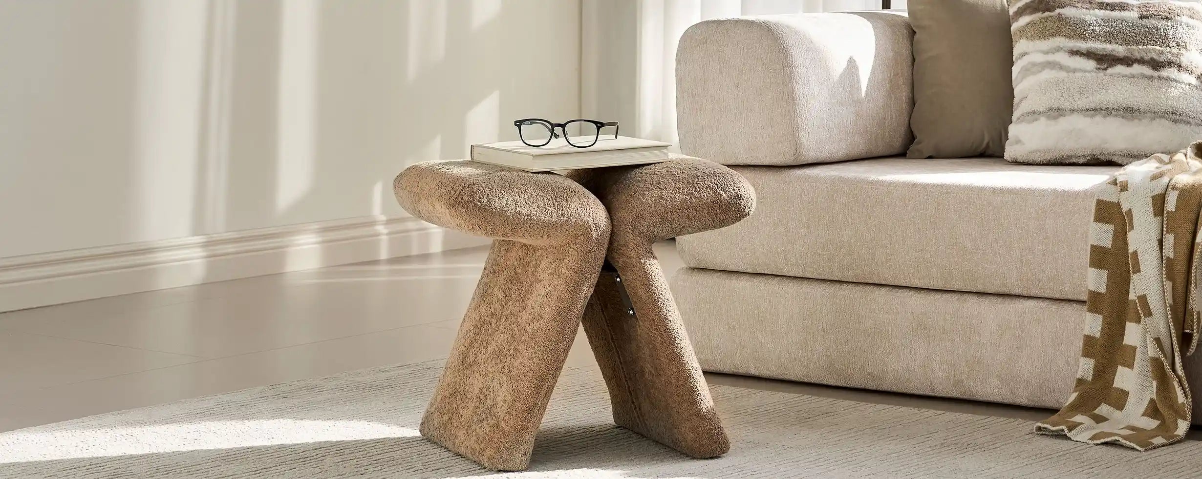 Faye Teddy Brown Accent Stool styled beside a sofa in a modern living room, used as a side stool with books and glasses