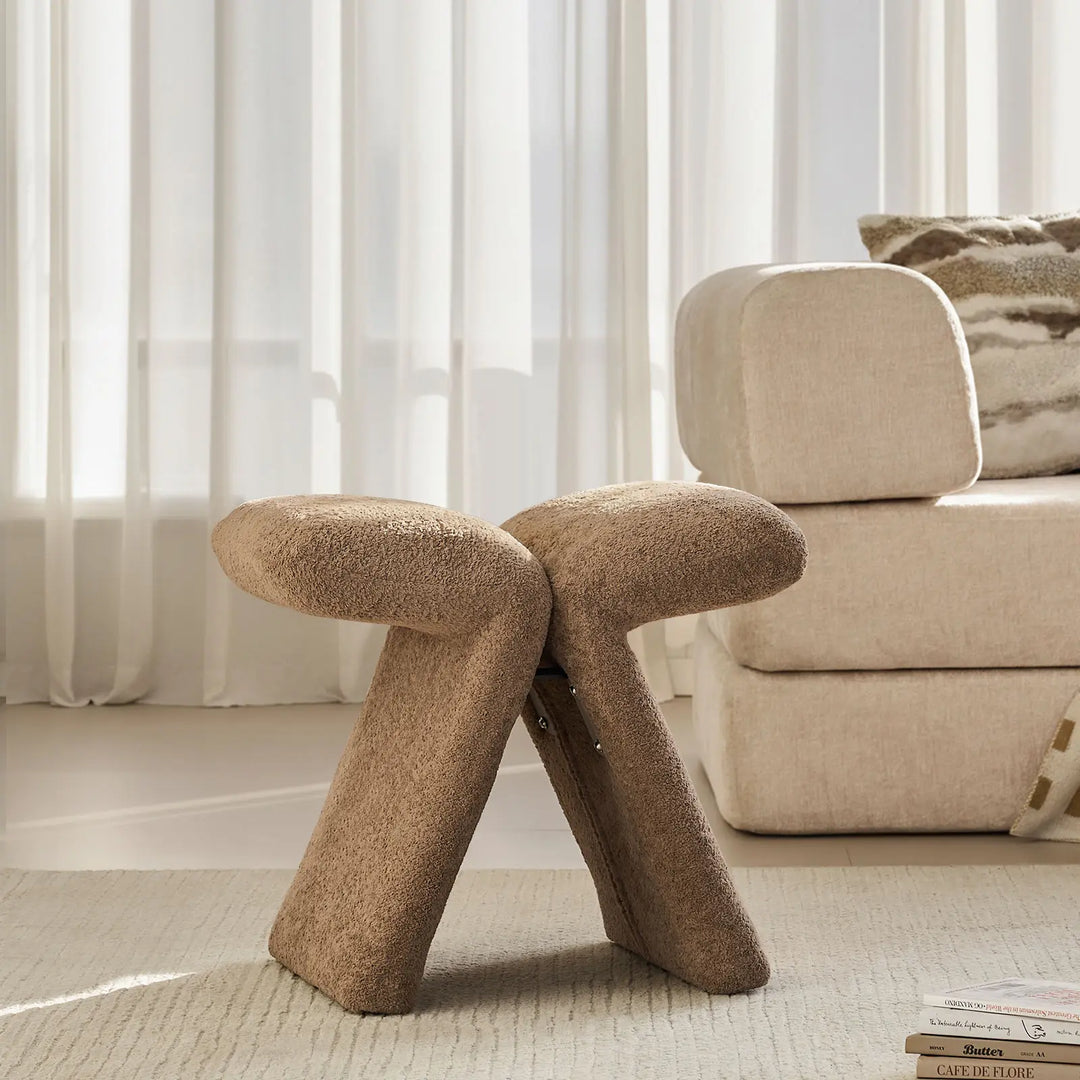 Faye Teddy Brown Accent Stool placed by the window next to a sofa in a contemporary living room