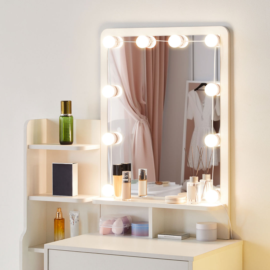 A closer view of the white dressing table, showing the details of the mirror and 10 LED bulbs, the tabletop and several shelves, in front of a white wall.
