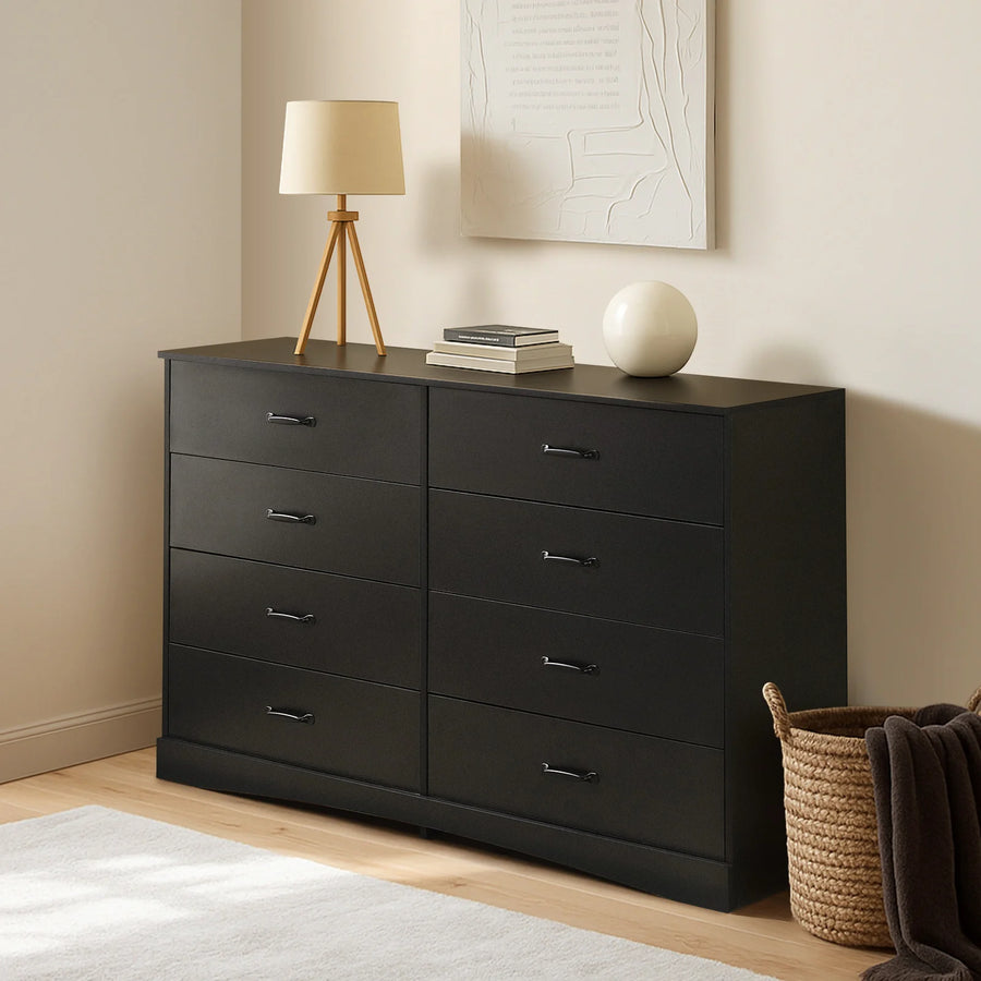Kamai black chest of drawers in warm bedroom, top surface with table lamp and stacked books