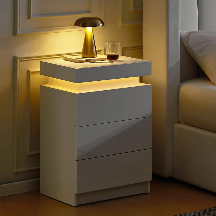 The side view of the white Kumar bedside table with RGB light strip, featuring 3 drawers, 1 hidden part, in a dark bedroom.