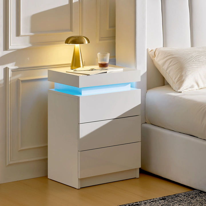 The side view of the white Kumar bedside table with RGB light strip, featuring 3 drawers, 1 hidden part, in a bright bedroom.