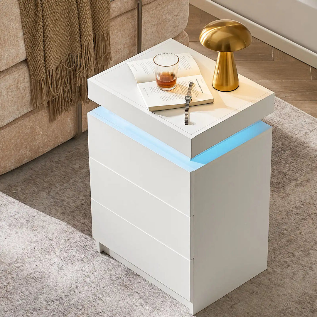 The view of the Kumar Bedside Table near the sofa, serve as a side table, featuring 3 drawers and a top that can be open, in a bright room.