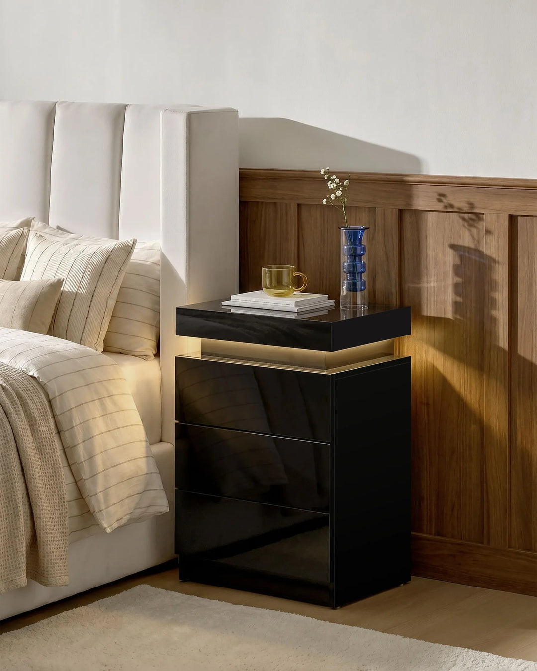 Black Kumar LED bedside table with warm ambient lighting beside a bed, modern high gloss LED nightstand for contemporary UK bedrooms