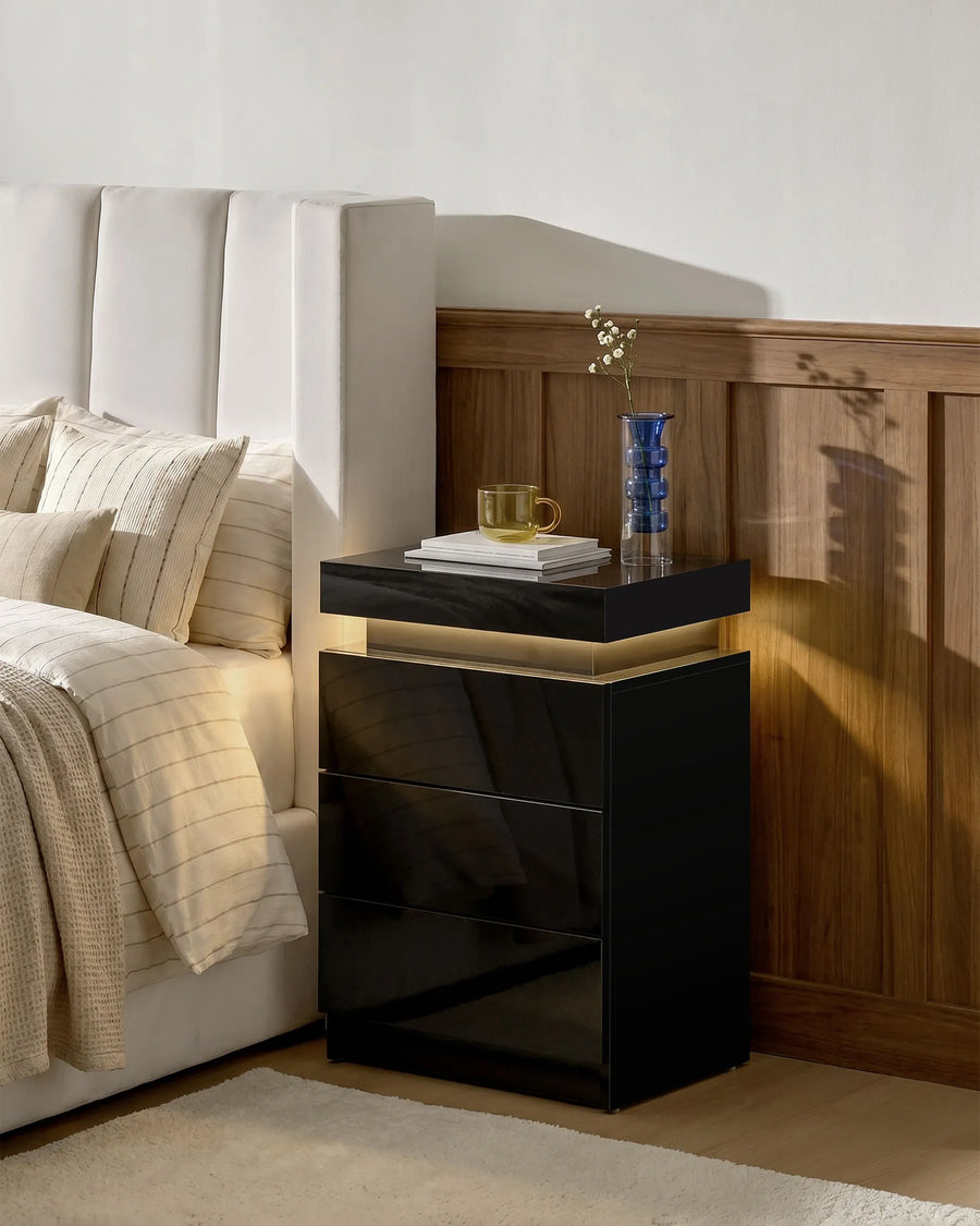 Black Kumar LED bedside table with warm ambient lighting beside a bed, modern high gloss LED nightstand for contemporary UK bedrooms